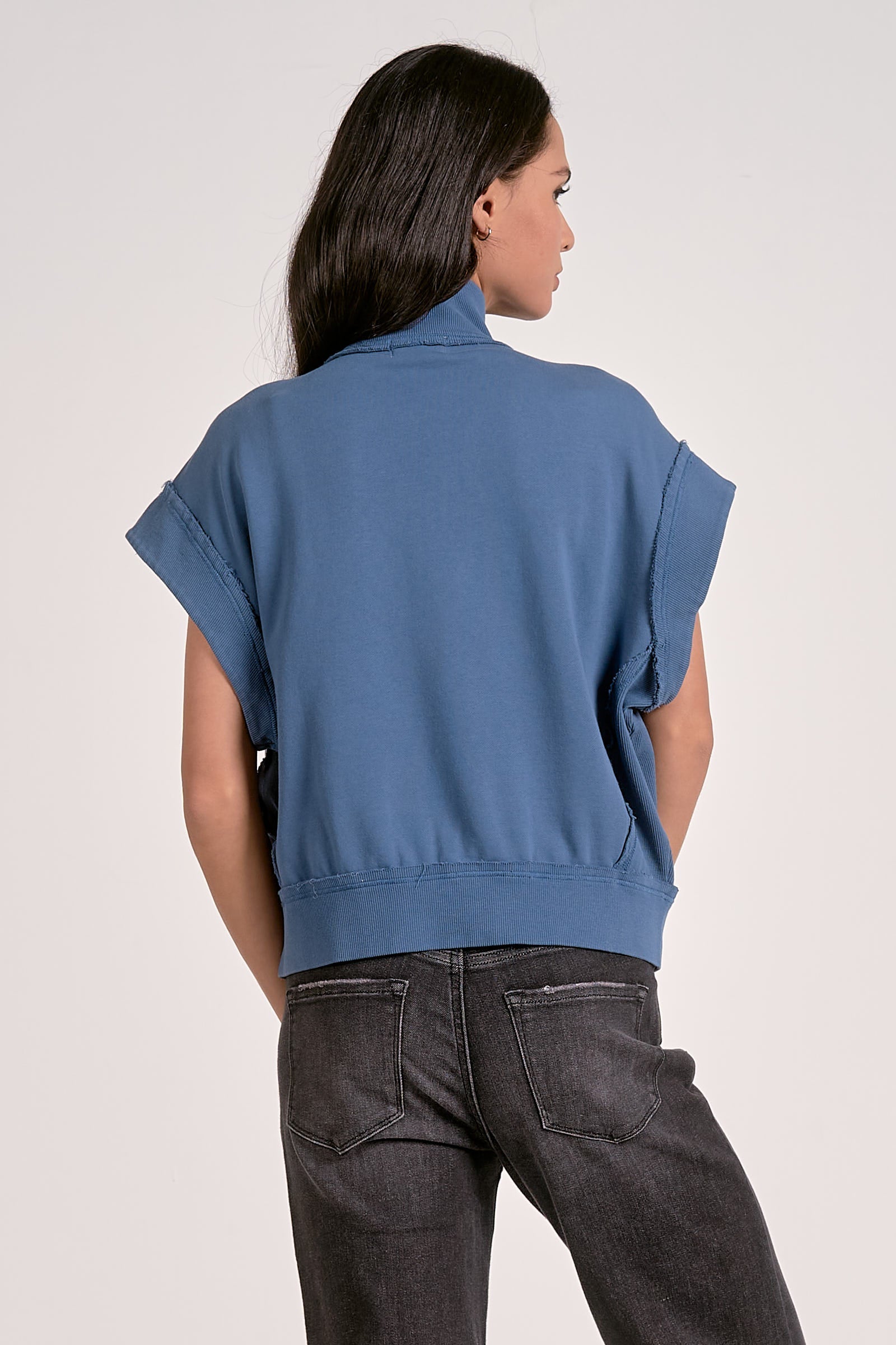 Person wearing a blue sleeveless top and dark jeans on a light background