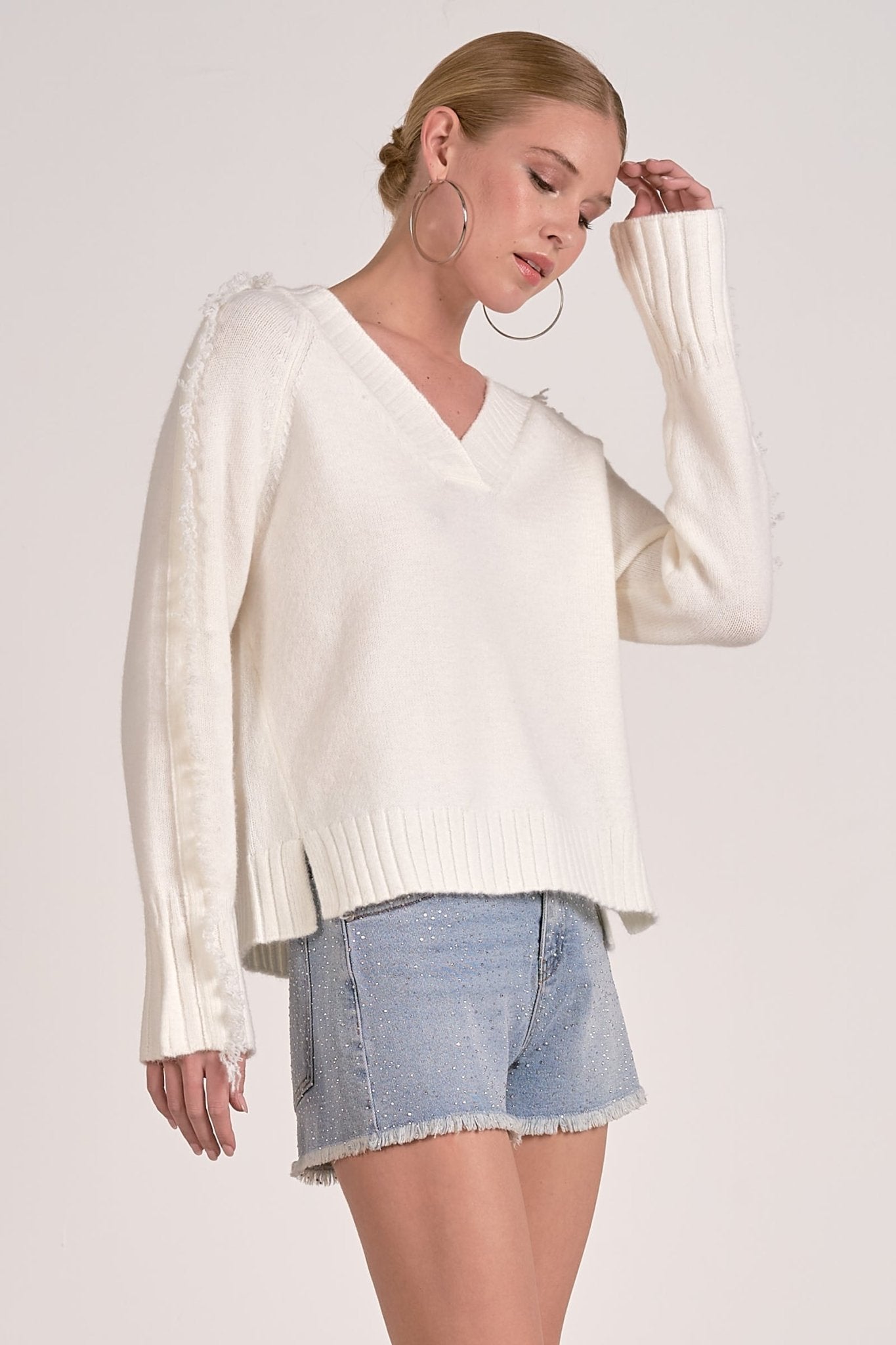 Model showing side of Willow Fringe V-Neck Sweater in ivory white with fringe trim sleeves from Mainstream Boutique Bloomington