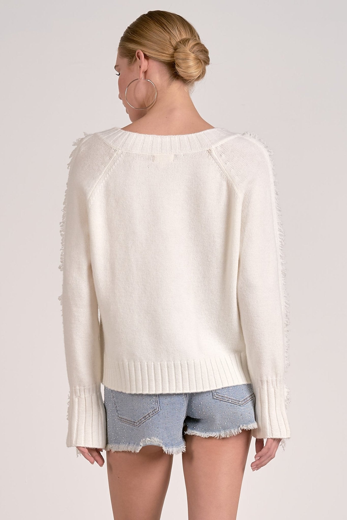 Model showing back of Willow Fringe V-Neck Sweater in ivory white with fringe trim sleeves from Mainstream Boutique Bloomington