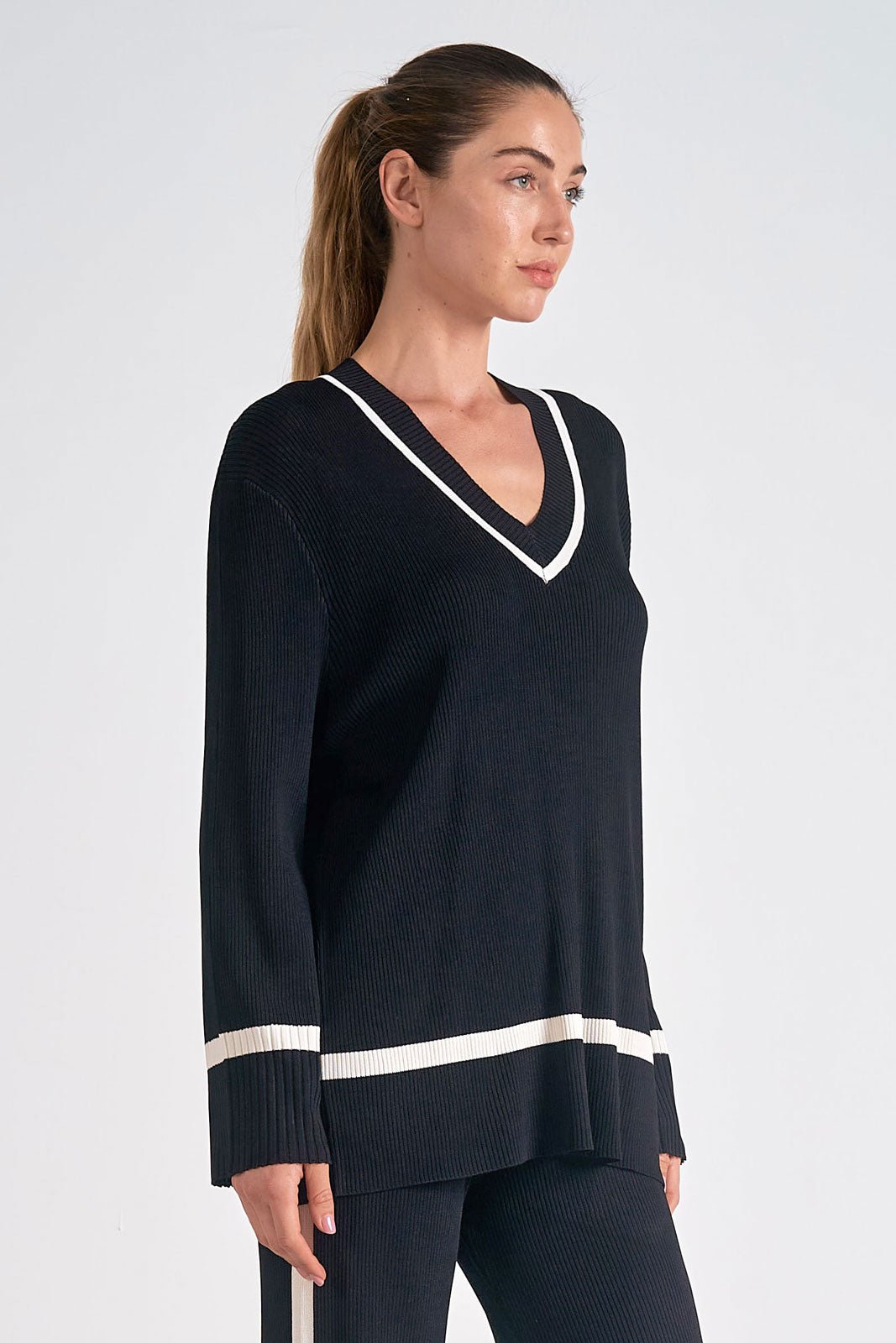 A woman wearing a black V-neck sweater knit track top with a ribbed design, featuring a loose fit and positioned against a white background.